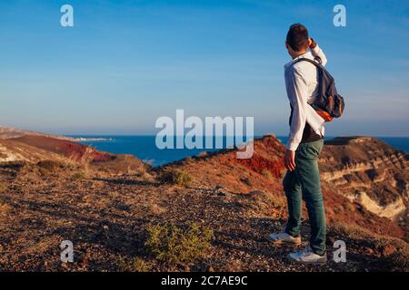 Hiker walking by White beach on Santorini island Greece enjoying sea mountain landscape. Man backpacker traveling Stock Photo