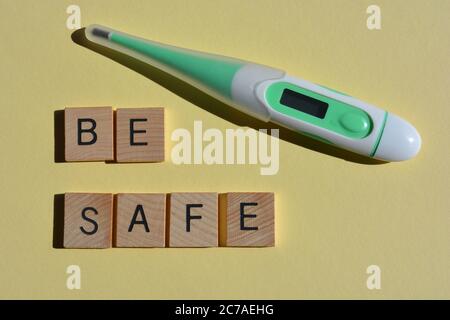Be Safe, words in wooden alphabet letters and a digital thermometer isolated on yellow background Stock Photo