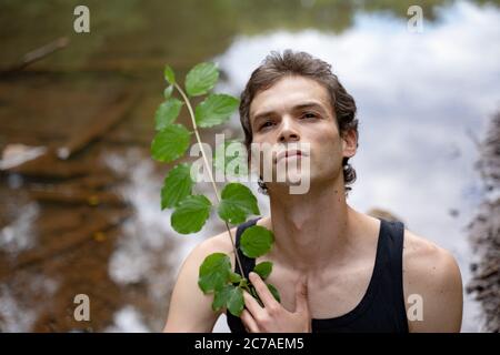 Close-up of thoughtful man holding plant against lake in forest Stock Photo