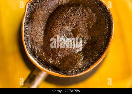 Natural coffee with thick foam, brewed in a copper cezve in the classical way, on a wooden background, macro photo. Stock Photo