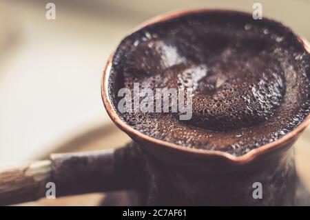 Natural coffee with thick foam, brewed in a copper cezve in the classical way, on a wooden background, macro photo. Stock Photo