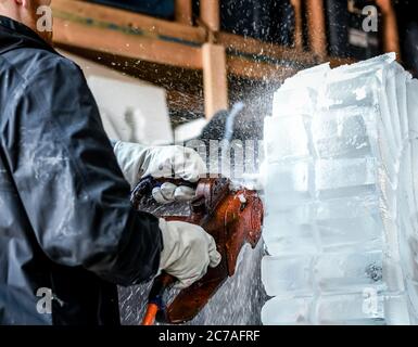 Ice carver sculpting block of ice with electric power chainsaw Stock Photo