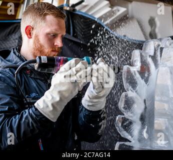 Ice carver sculpting block of ice with electric power dremel Stock Photo