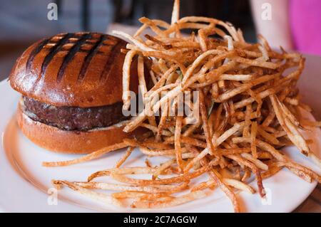 juicy beef burger on brioche buns with shoestring potato french fries on a white plate Stock Photo