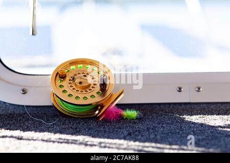 A fly fishing reel with bright green line sits on the deck of a boat, ready for an Alaskan fishing adventure in pristine waters. Stock Photo