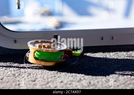 A fly fishing reel with bright green line sits on the deck of a boat, ready for an Alaskan fishing adventure in pristine waters. Stock Photo