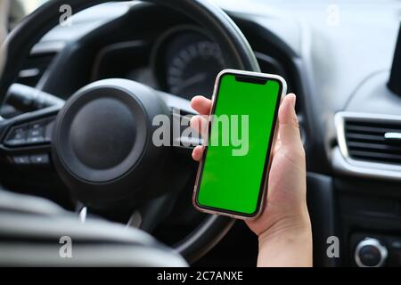 over shoulder of man holding green screen smart phone in the car. blur background Stock Photo