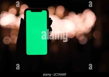close up one hand showing green screen smart phone at night. Beautiful golden bokeh background Stock Photo