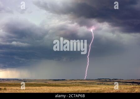 Powerful lightning bolt from a thunderstorm with dark rain clouds and stormy sky near Hartley, Texas Stock Photo