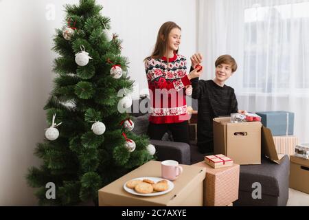 Portrait of beautiful young couple sitting on sofa at home and happily decorating Christmas tree together Stock Photo