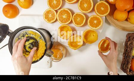Freshly squeezed orange juice. Caucasian woman squeezing oranges using electric juicer. Close up on white background, view from above Stock Photo