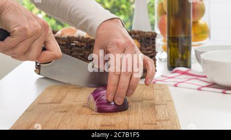 Woman chopping red onion on a wooden chopping board close up on a kitchen table Stock Photo