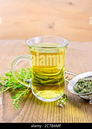 Herbal tea in a glass mug of thyme, metal strainer with dry leaves, a bunch of fresh savory on the background of an old wooden board Stock Photo