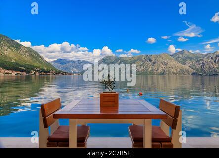 Waterfront table at a restaurant with a view of Kotor Bay of Kotor Bay or Boka Kotorska in the background in Montenegro, on the Adriatic Sea Stock Photo