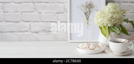 Tea in a cup with a golden strainer. Bizet on a plate. Frame with dried flowers. Aged white brick background. Green hydrangea in a vase in the Nordic Stock Photo