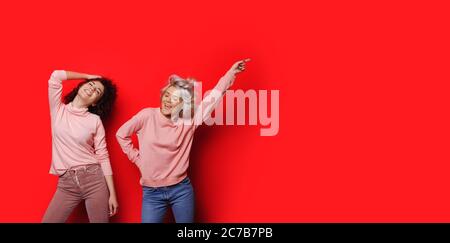Charming ladies with curly hair dancing on a red wall with free space pointing to that Stock Photo