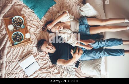 Upper view photo of a caucasian couple lying in bed and studying while eating cereals with milk Stock Photo