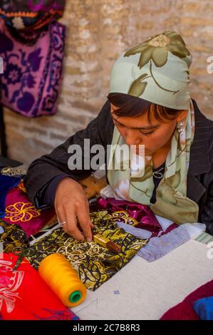 A young Uzbek woman is doing embroidery in a bazaar (a market in a Middle Eastern country) in Bukhara, Uzbekistan. Stock Photo