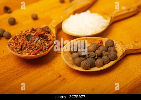 Black allspice, coarse salt and various ground spices in wooden spoons on a wooden Board. Close up Stock Photo