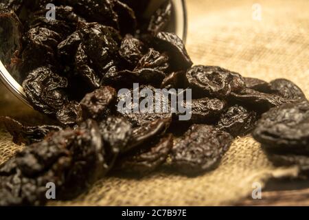 Dried prunes spilled from a metal bowl on a wooden background. Close up Stock Photo