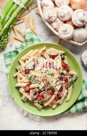 Penne pasta with green asparagus, parma ham and mushrooms in a cheese sauce. Topped with parmesan cheese Stock Photo