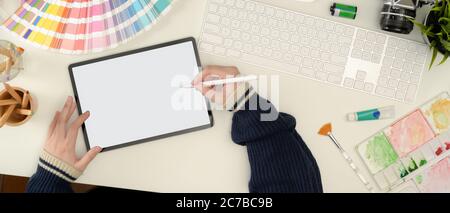 Overhead shot of female designer working on mock up tablet with stylus pen on white worktable with painting tools Stock Photo