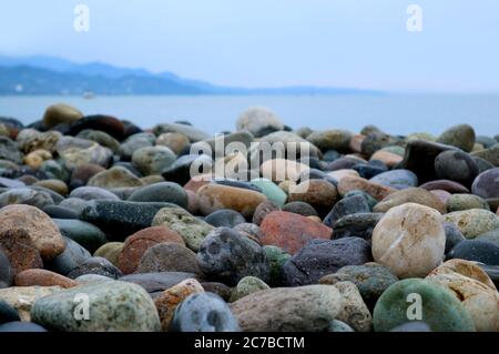 Closeup Multi-color Natural Pebble Stones on the Beach with Blurry Seascape in the Backdrop Stock Photo