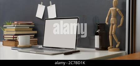 Side view of study table with mock up laptop, stack of books and decorations on white desk Stock Photo