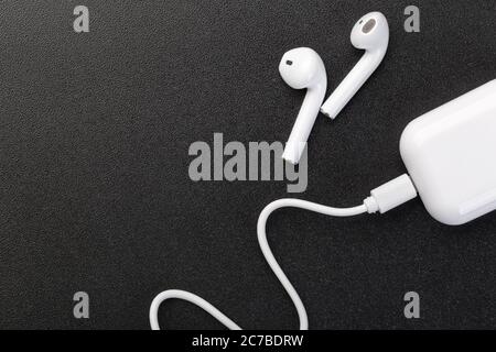 Modern wireless bluetooth headphones with charging case on a dark black background. The concept of modern technology, gadgets. Stock Photo