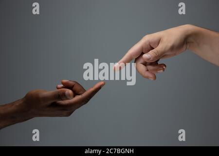 Touching of God. Racial tolerance. Respect social unity. African and caucasian hands gesturing on gray studio background. Human rights, friendship, intenational unity concept. Interracial unity. Stock Photo