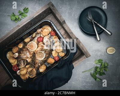 Roasted sea breams - dorado sea fish with tomato and potatoes on baking pan. Traditional mediterranean cuisine. Overhead view. Stock Photo