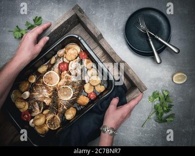 Roasted sea breams- dorado sea fish with tomato and potatoes on baking pan. Traditional mediterranean cuisine. Overhead view. Stock Photo
