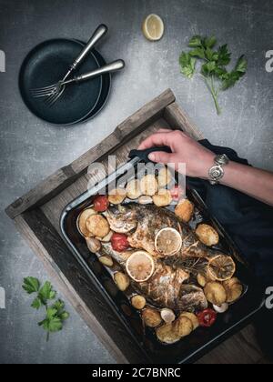 Roasted sea breams - dorado sea fish with tomato and potatoes on baking pan. Traditional mediterranean cuisine. Overhead view. Stock Photo