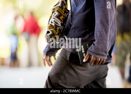 Close shot of a male holding a bible walking in the street with a blurred background Stock Photo