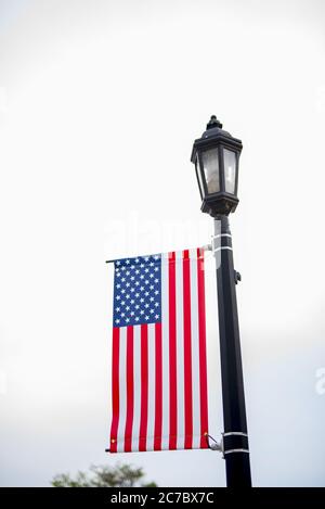 Vertical shot of united states flag hanging from a lamp post with a cloudy sky in the background Stock Photo