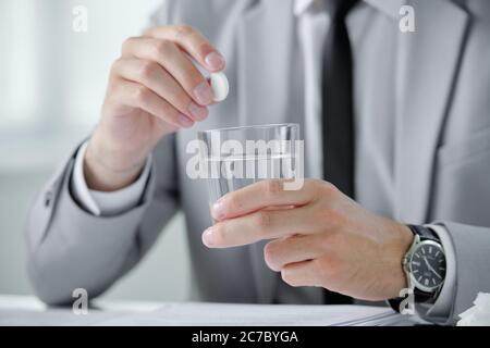 Close-up of unrecognizable businessman in wristwatch dissolving pill into water while suffering from morning hangover at workplace Stock Photo