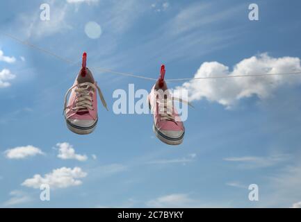 old pink sneakers dry on clothespins on a rope against a background of blue sky  Stock Photo