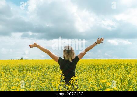 A young woman with raised arms stands in a field with flowering plants summer day. Happiness informative detox concept. Stock Photo