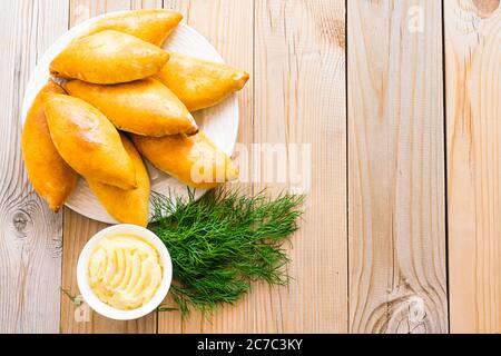Small pies with a crispy golden crust of potato filling lie in a heap plate wooden background. Homemade country baking Stock Photo