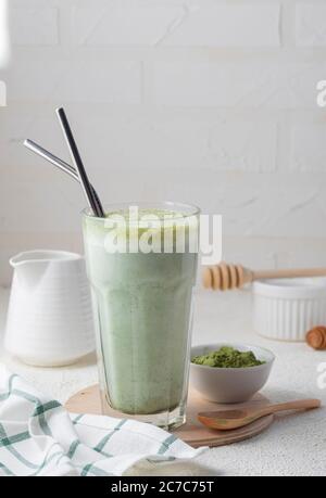 Selective focus, hot matcha tea, latte, in a high transparent glass and metal tubes, with milk, in a home interior with white dishes Stock Photo