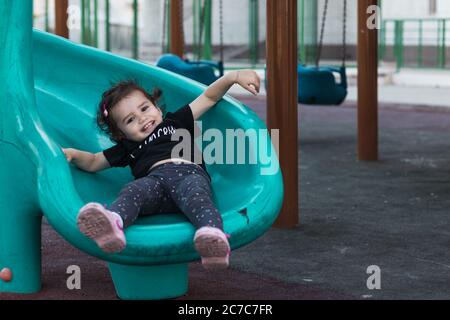 a happy little girl sliding down the blue slide in a playground. Stock Photo