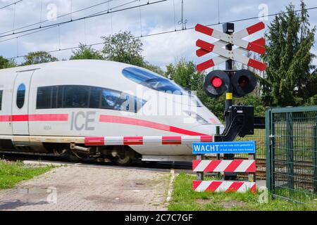 Bennekom-Netherlands,Juli 11,2020:German ICE train passing a closed railway crossing with closed barriers blinking red lights. Warning sign text Wait Stock Photo