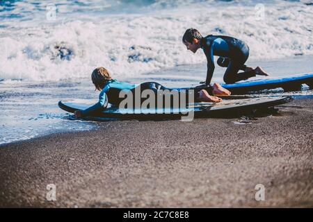 kids enjoying a funny surf day in the shore of a sunny beach in their coastal holidays Stock Photo