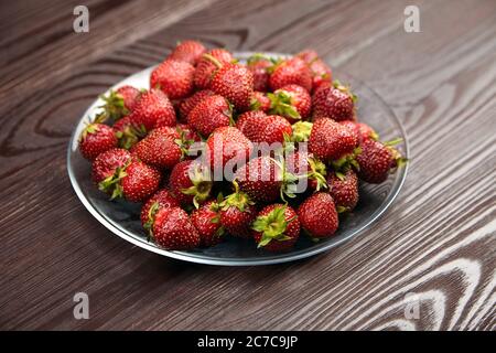 Strawberries on a transparent glass plate on wooden background. Red ripe berries, fresh juicy strawberries Stock Photo