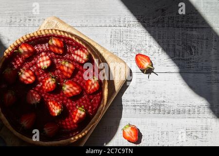 Homemade strawberry pie decorated with fresh berries on light wooden table background with falling shadows, top view Stock Photo