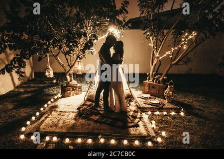 Horizontal shot of a man and a woman standing in front of a tent in a garden during nighttime Stock Photo