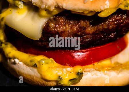 Detail of beef cheeseburger with melted cheese isolated on black background. Stock Photo