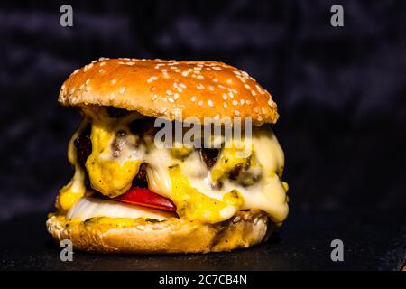 Detail of beef cheeseburger with melted cheese isolated on black background. Stock Photo