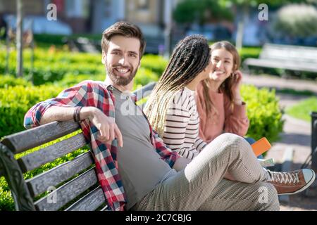 Young attractive guy posing and two girls on bench. Stock Photo