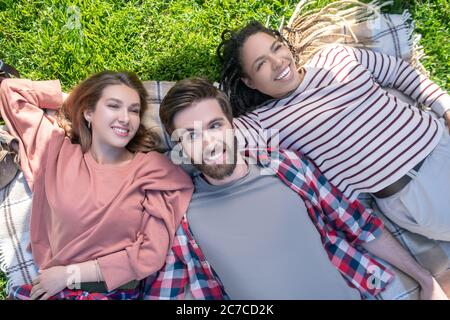 Guy and two girls lying on a plaid on grass Stock Photo